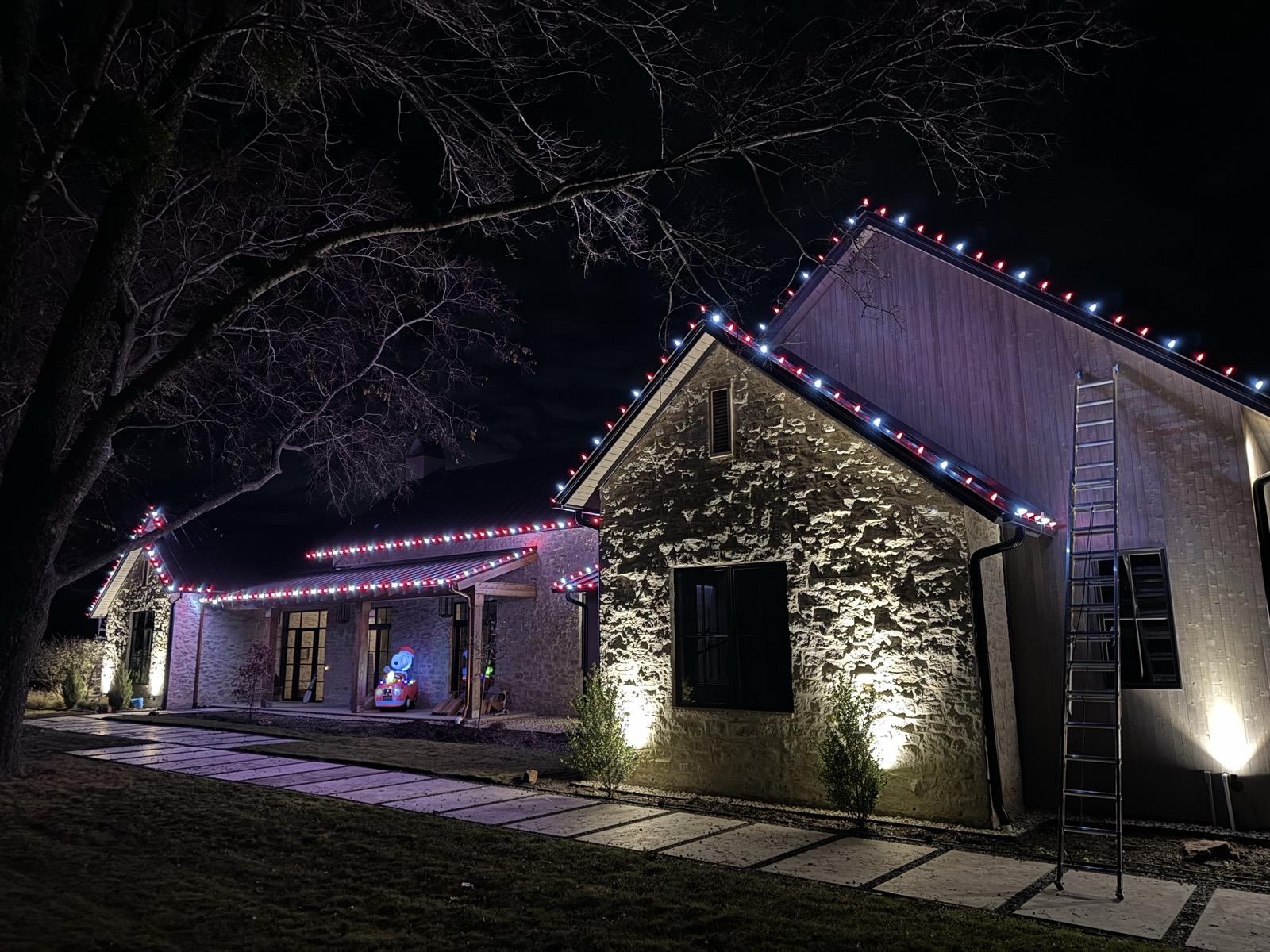 Stone home with red and white roofline lighting and uplit stone facade