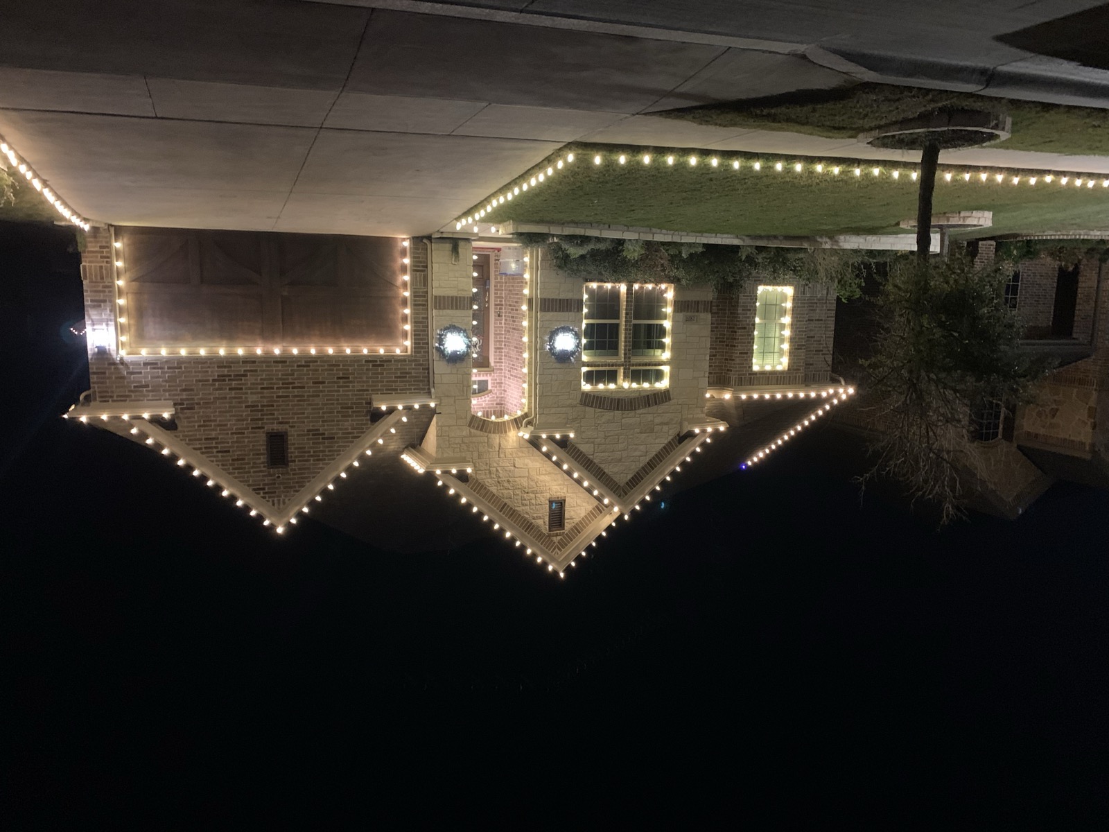 Brick home with warm white roofline lighting, landscape bed border lights, and matching wreaths